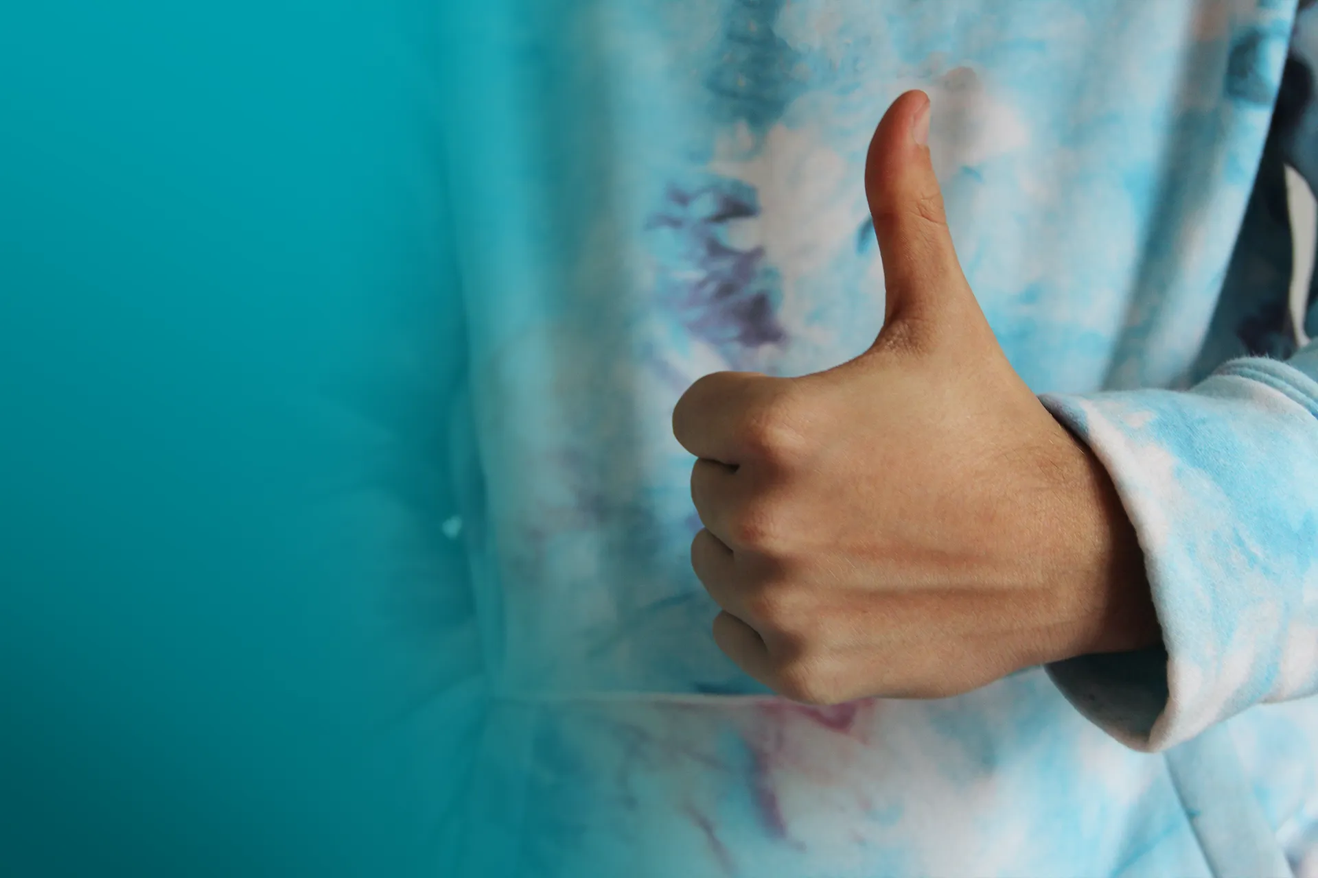 Person in tie-dye sweater giving a thumbs-up